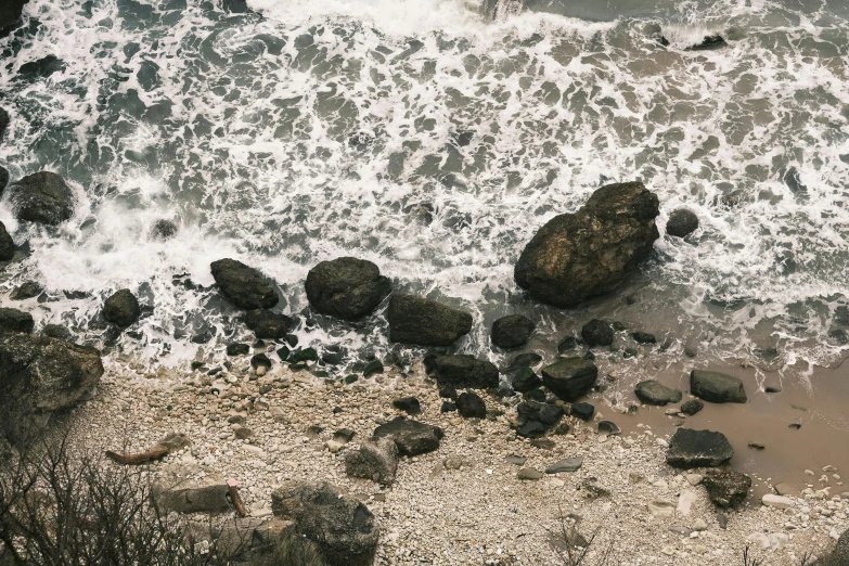 an overview of a rocky shoreline with rough, sandy, and gray waves