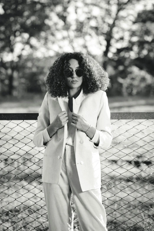 black and white pograph of woman in white coat standing by fence