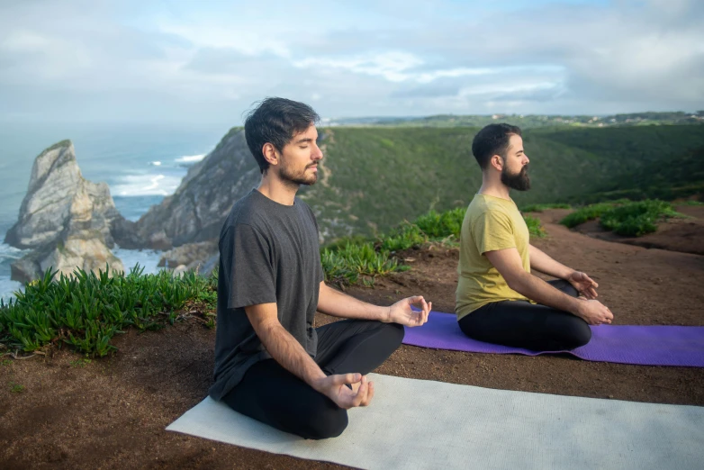 two men sitting on yoga mats with the ocean in the background