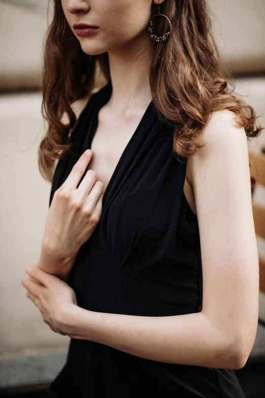 the woman wears a black dress and her hand on her chest