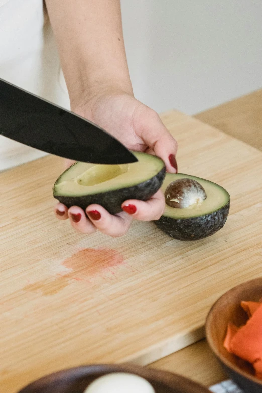 someone holding a knife in their left hand slicing an avocado