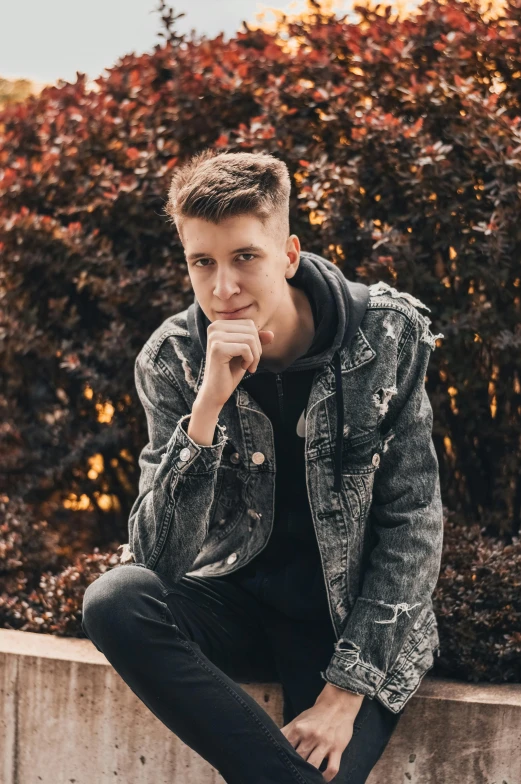 a young man with a jean jacket sitting on a ledge