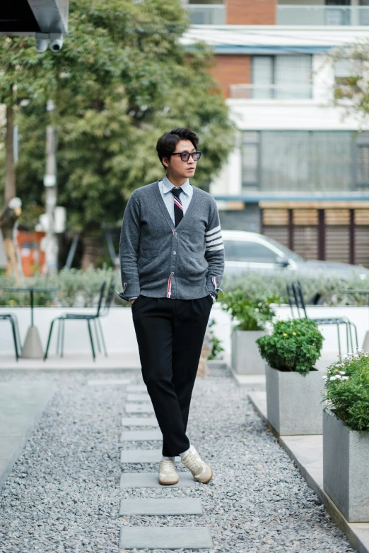 a young man wearing glasses and a sweater walks down the street