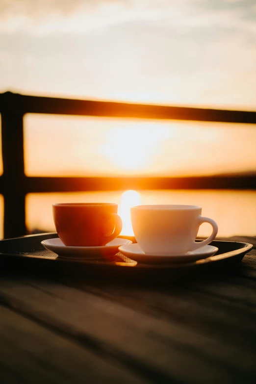 two cups of coffee on a plate are sitting on a wooden table