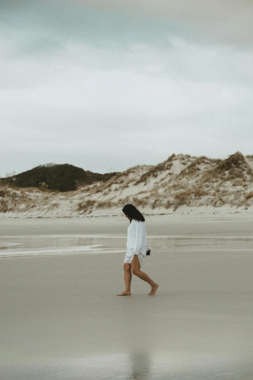 a woman walking across a sandy beach covered in sand dunes