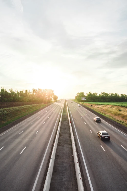 three cars are driving on the highway as the sun sets