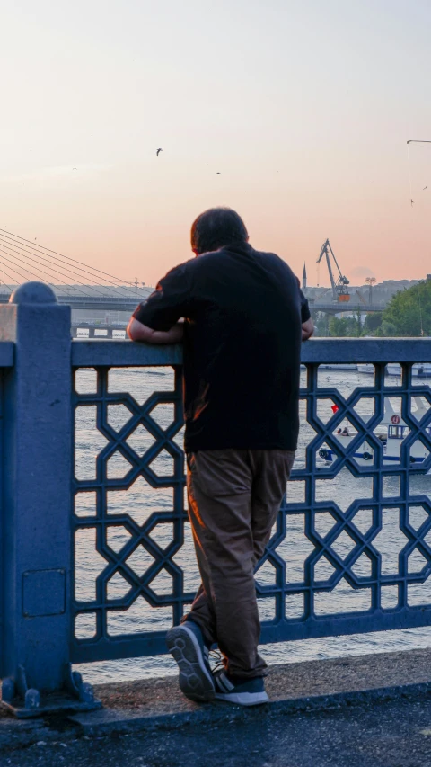 the man is leaning against a metal fence looking out onto a large body of water