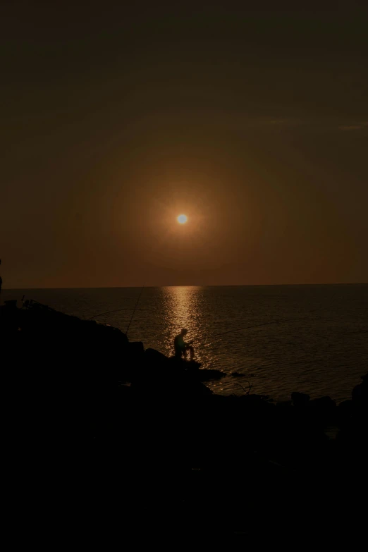 a sun is setting over the ocean with people in silhouette