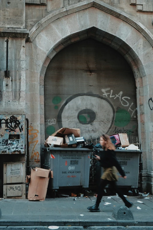 a woman running down the street near garbage cans and bins