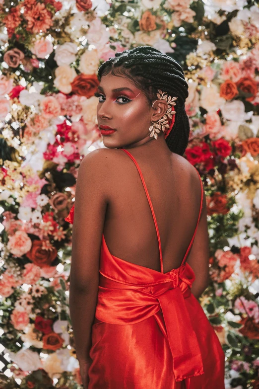 a woman in red dress and large earrings standing in front of flowers