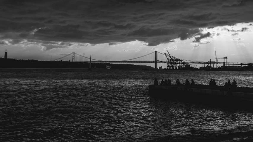 a boat sails past a bridge under dark clouds