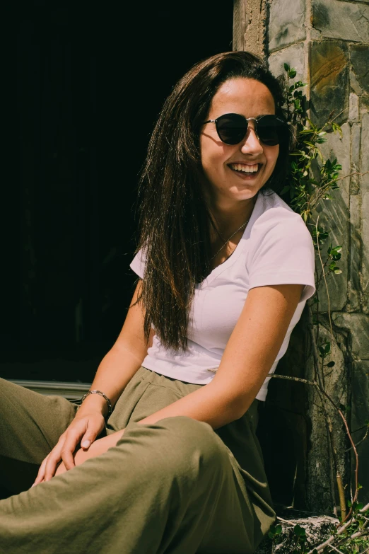 a smiling girl in sun glasses sitting on stone wall