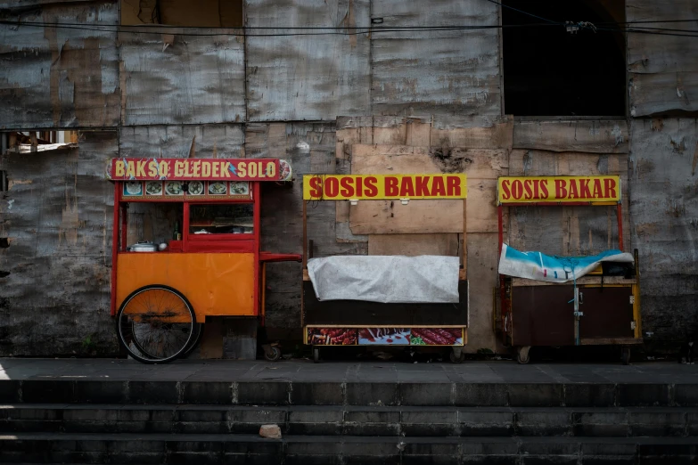 there are two wooden chairs and an orange cart in front of a building