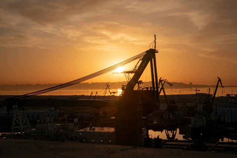 the sun sets behind a crane in a harbor