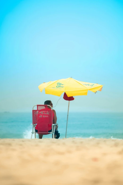 a man sitting on top of a red chair under a yellow umbrella