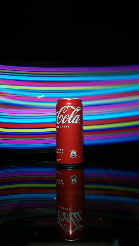 a red can of drink standing in front of a background with colorful strips