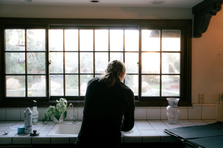 a man standing at the sink in the kitchen looking out a window