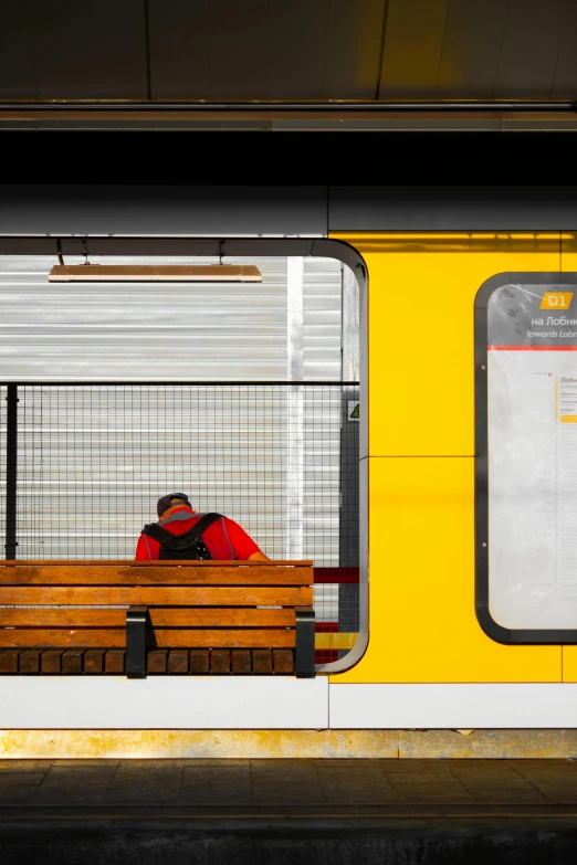 the person is sitting on the bench at the train station