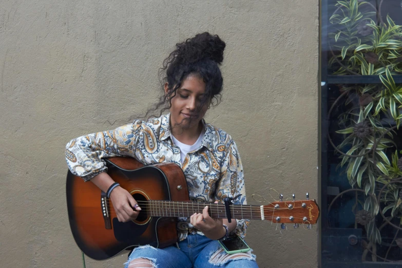 a woman sitting on a ledge playing a guitar