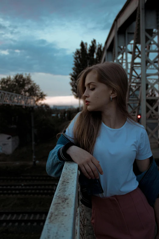the girl is sitting on the rail near a bridge