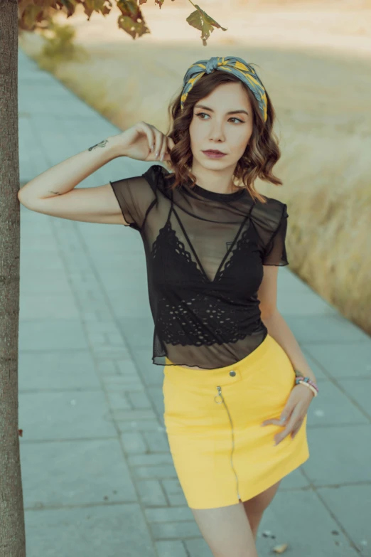 a young lady in a yellow skirt stands near a tree