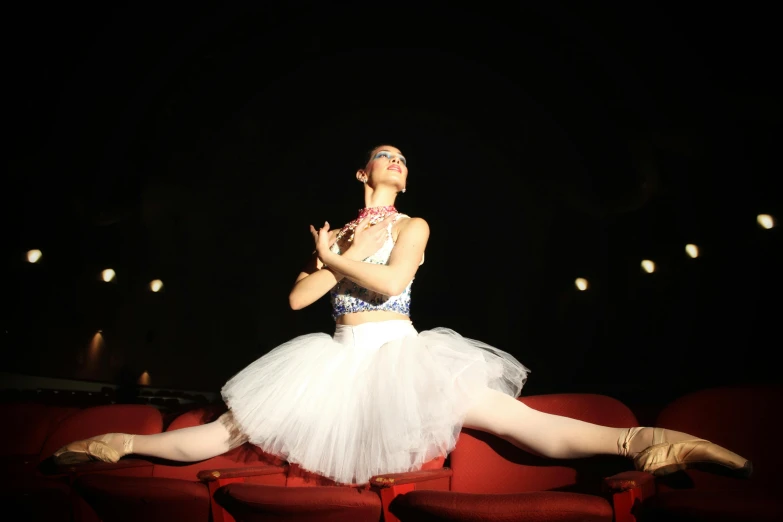 a young ballerina in white dress on red theater seats