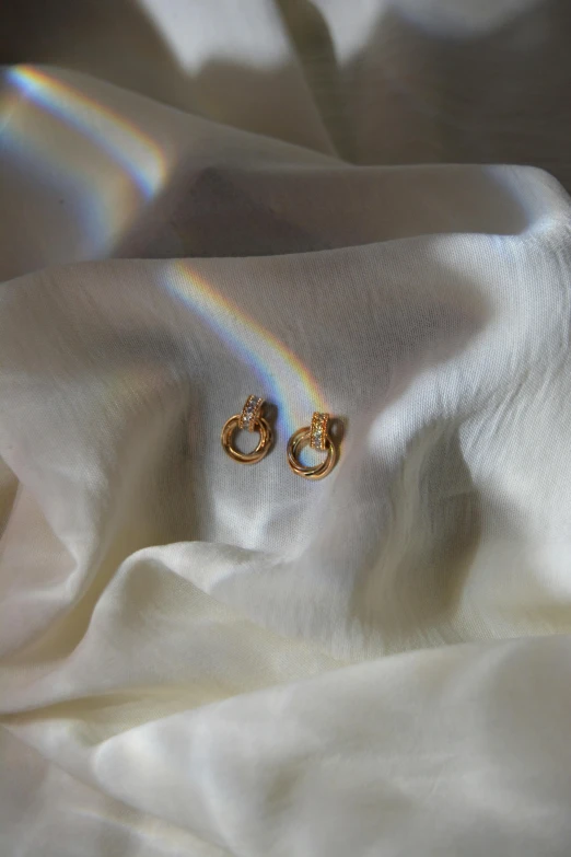 a couple of golden earrings are on a white fabric