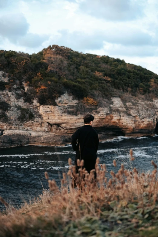 a man is walking on a hillside with a rock face in the background