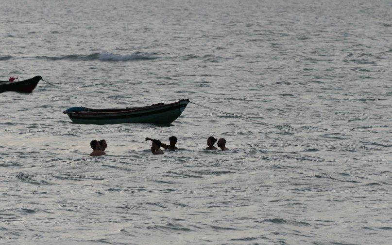 several people in the water with two small boats in the background