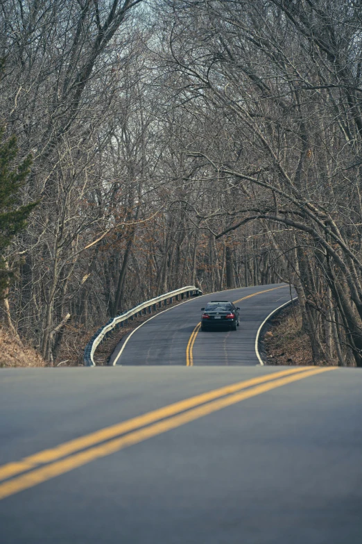 two cars driving down a road near a tree covered hillside