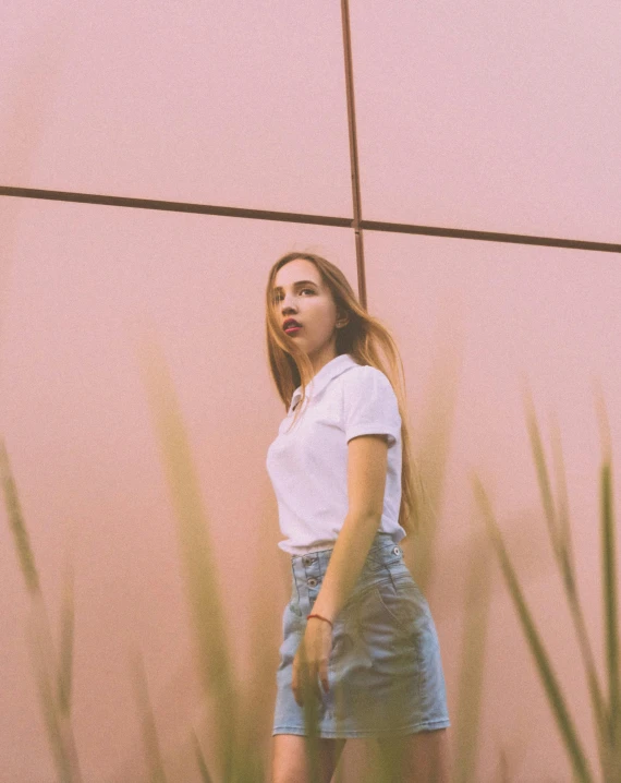 a woman walking by a fence with high grass behind her