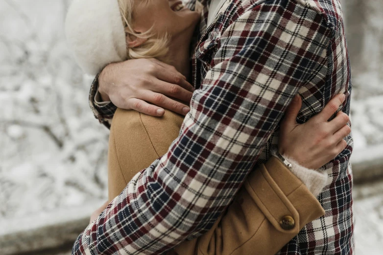 man and woman with their arms around each other with snow on trees in the background