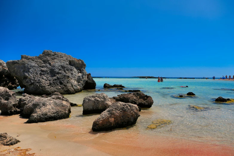 the beach with rocks, blue water and boats are in the distance