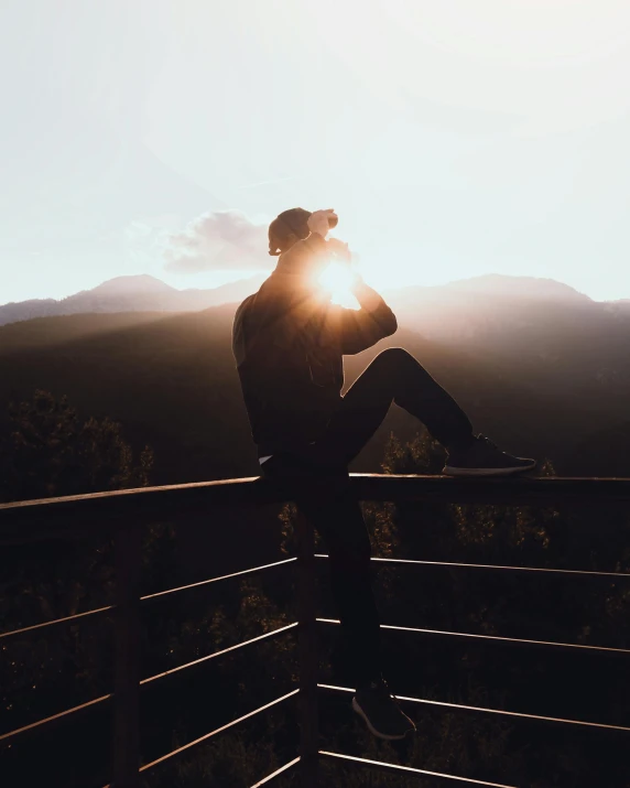 person sitting on fence overlooking valley at sunset