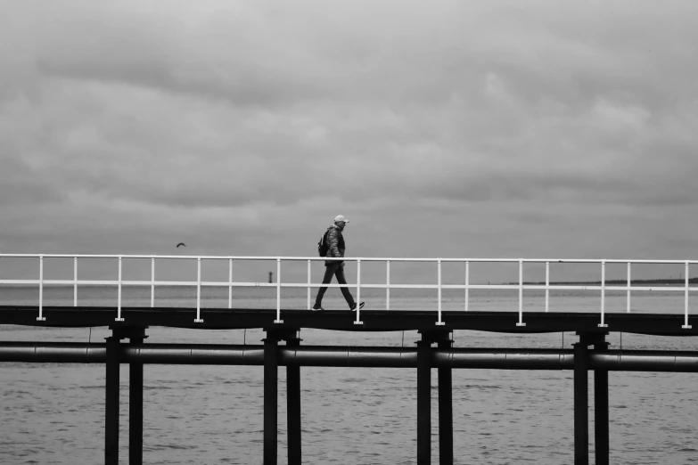 a man walking across a wooden bridge near the ocean