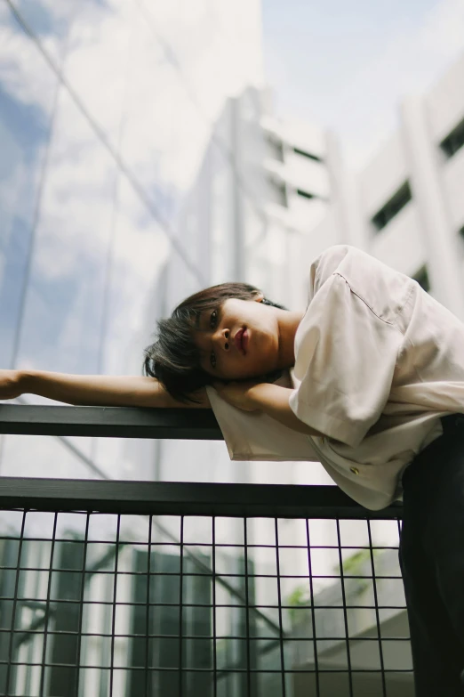 a young woman wearing a white shirt leans against a railing on a street