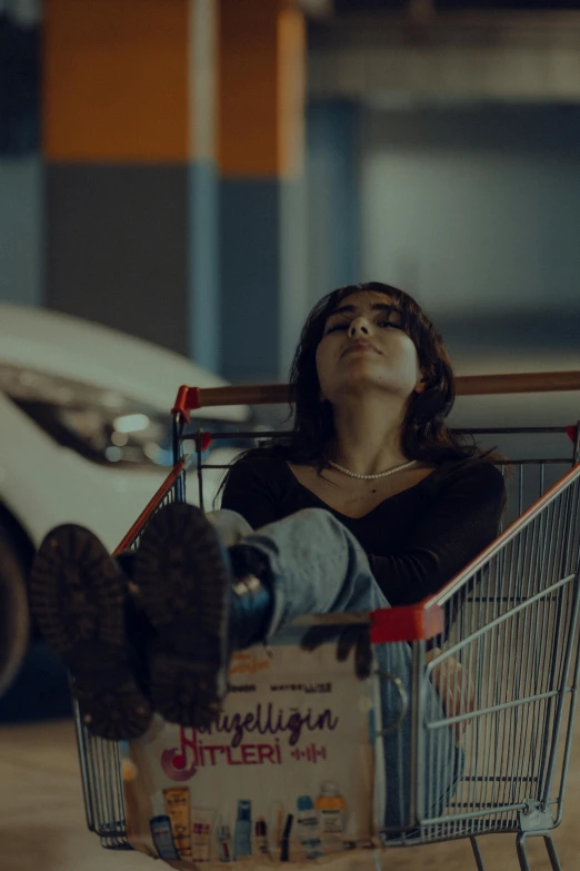 woman lying face down on top of a shopping cart and reaching up with both hands