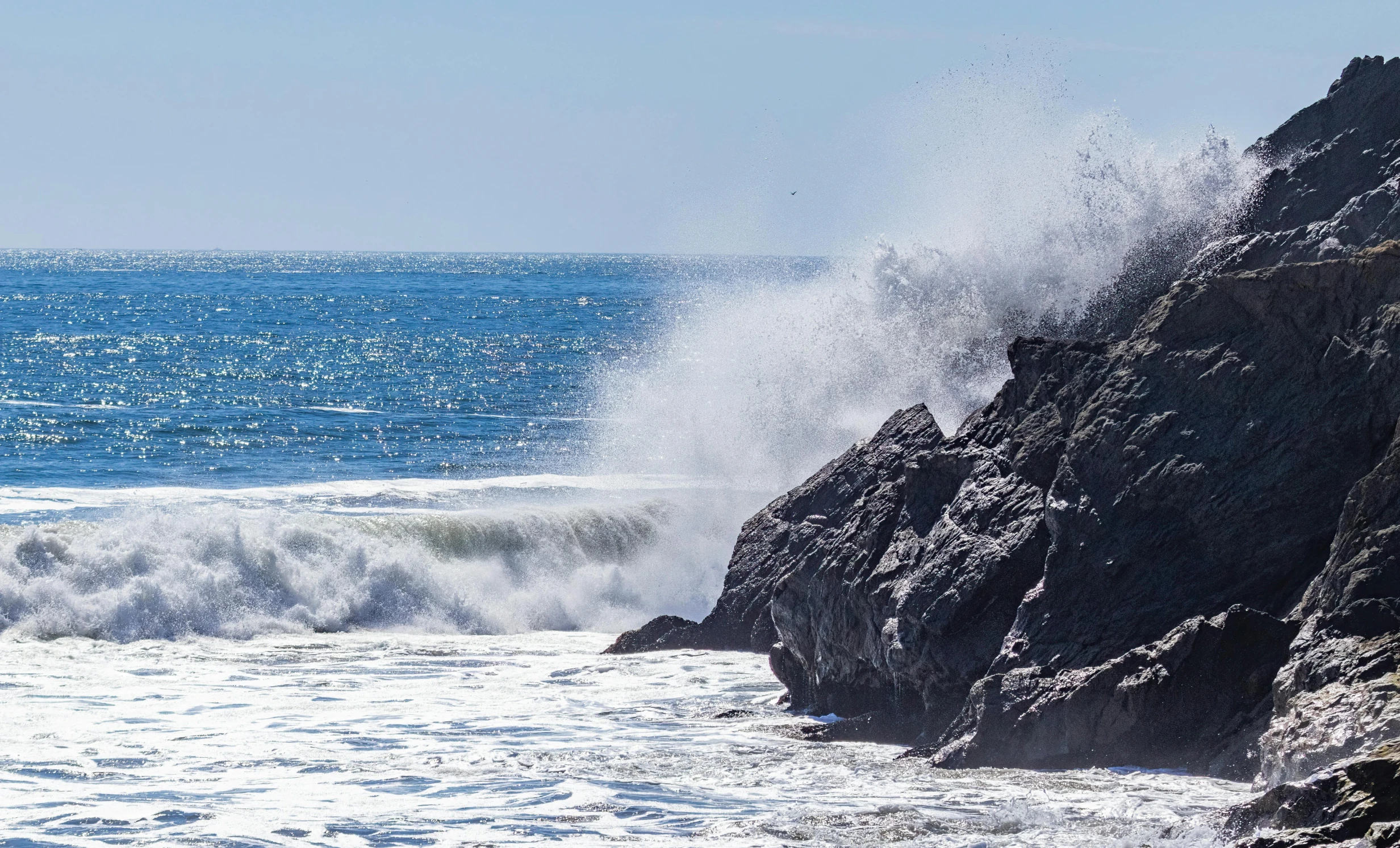 a large wave breaking on rocks with water crashing down