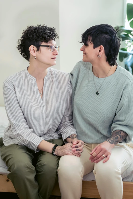 two woman sit on a bed while one looks at each other