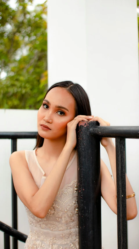 a woman in a white dress leaning on a gate