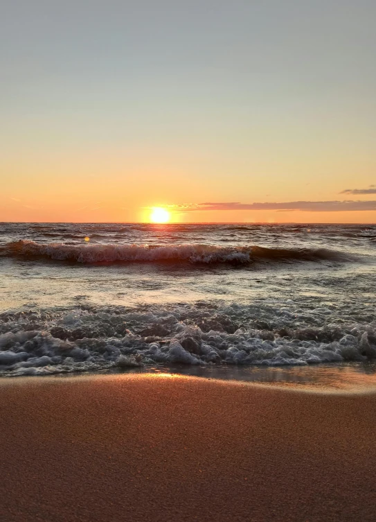 the sun is setting at the beach as waves come in