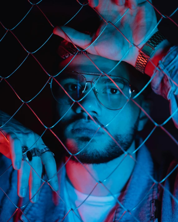 a man is wearing glasses and a blue light behind a fence