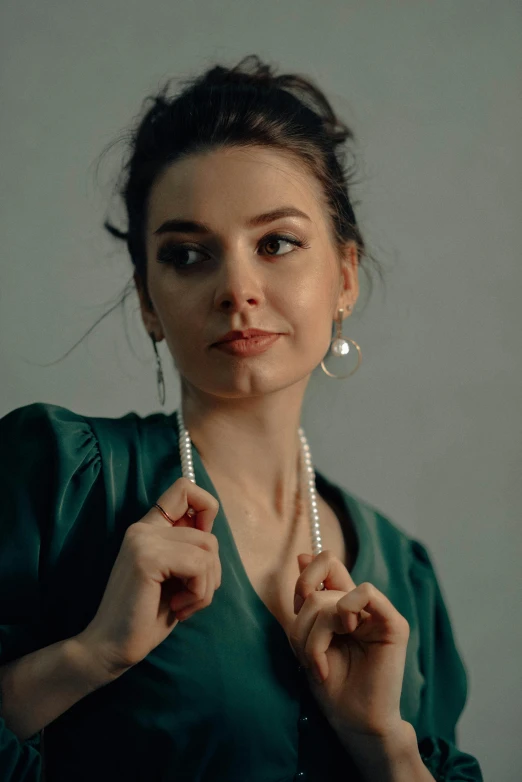 the woman is dressed in green, and holds a pearl necklace