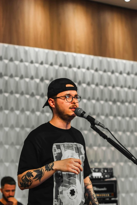 a male with glasses and a cap is singing in front of an audience