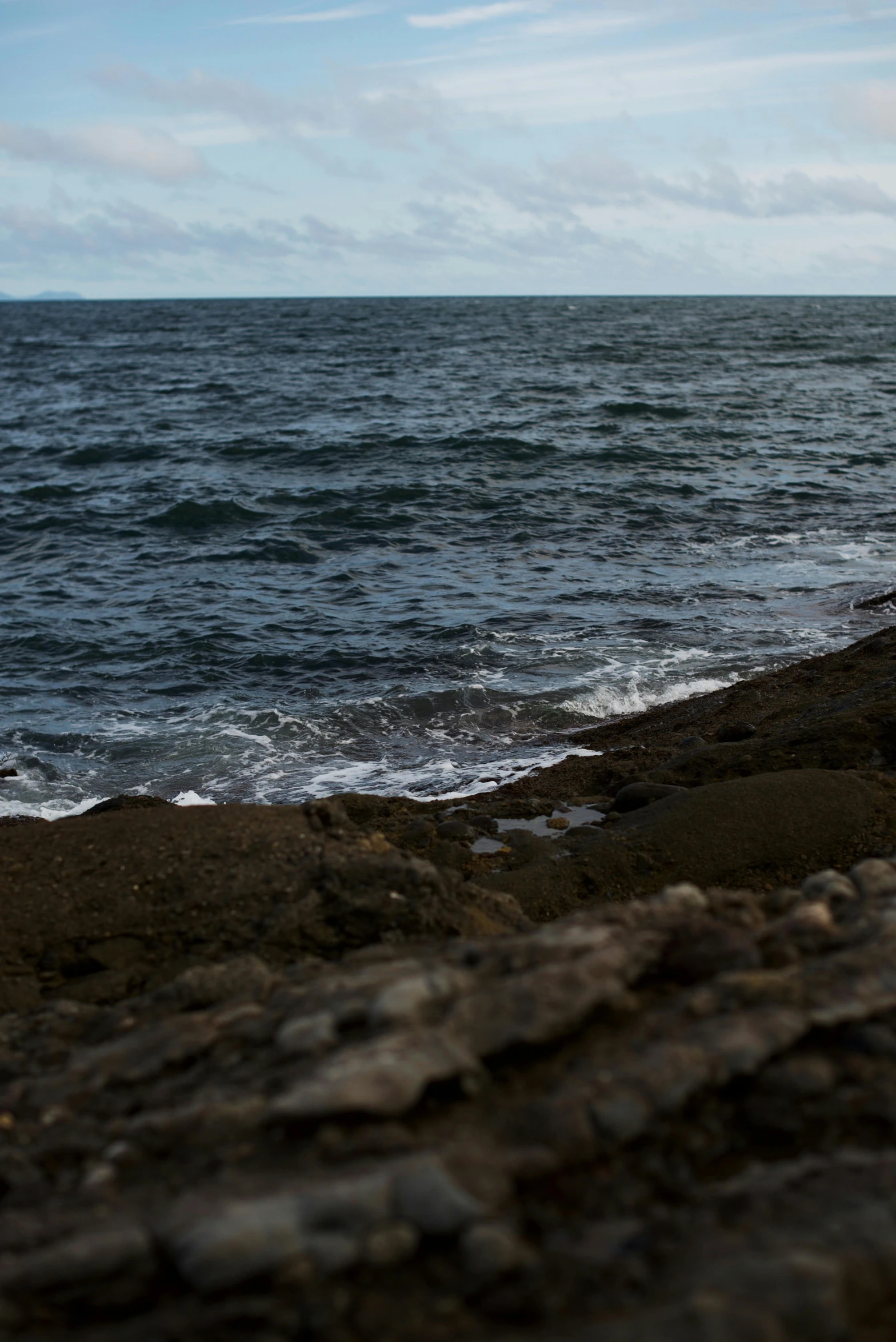 an ocean with waves crashing in to the shore and a single beach toy laying on a rocky area with stones