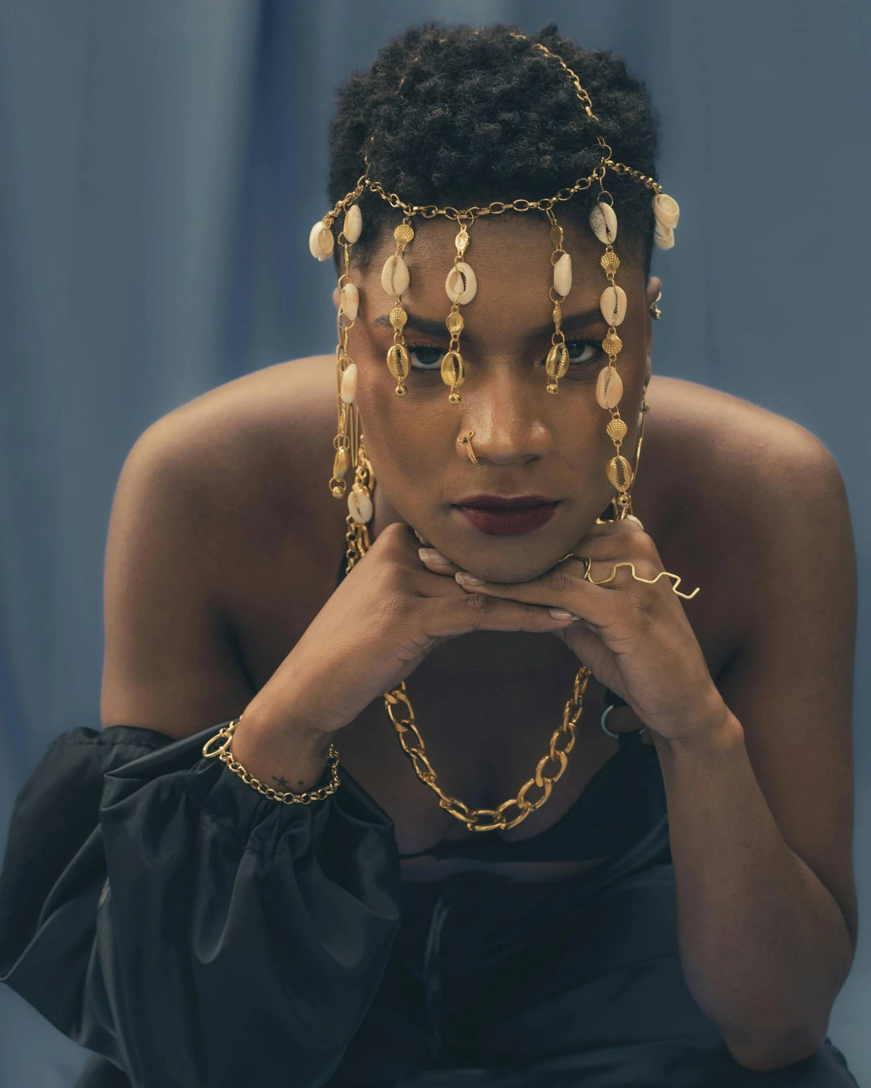 a woman sitting wearing gold necklaces and matching pearls