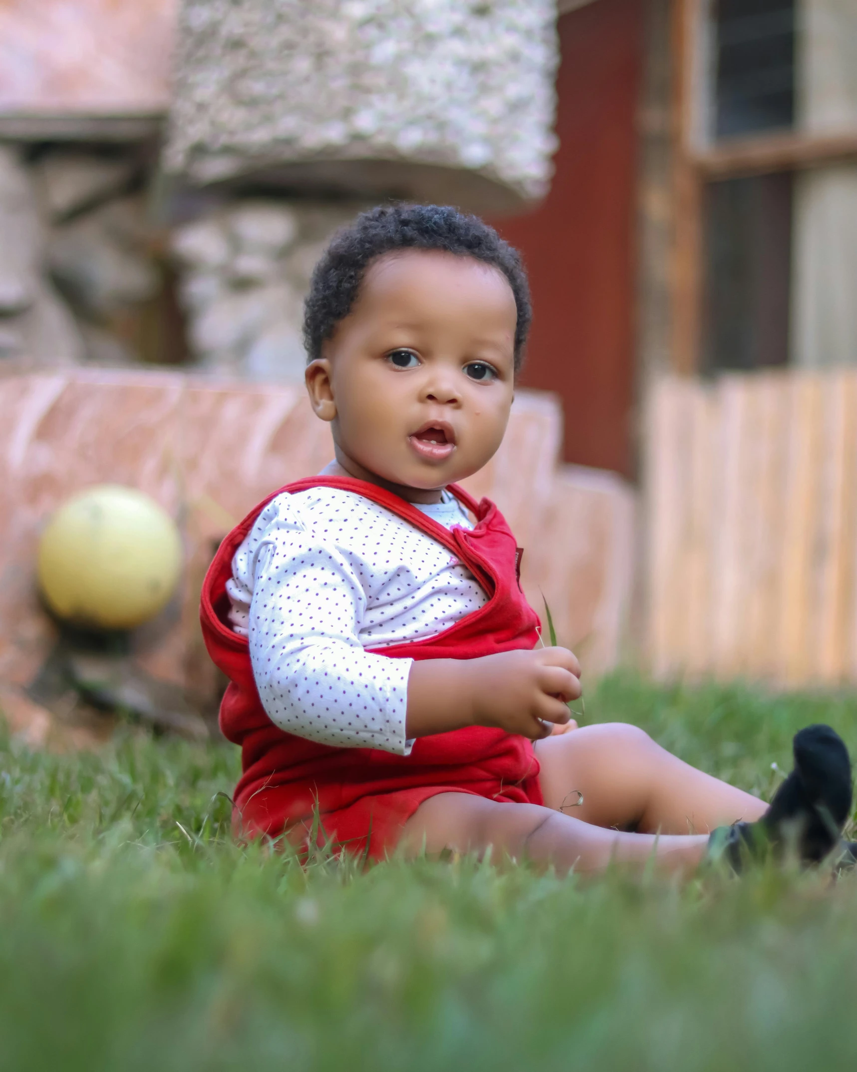 small black child sitting in grass with ball in background