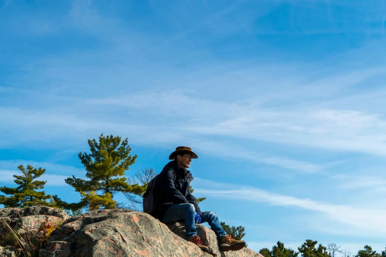 the man sits on a large rock and looks up at the sky