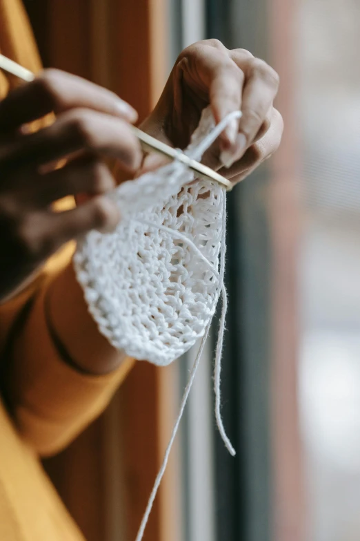 a woman holding a white piece of crochet with a white knitting needle