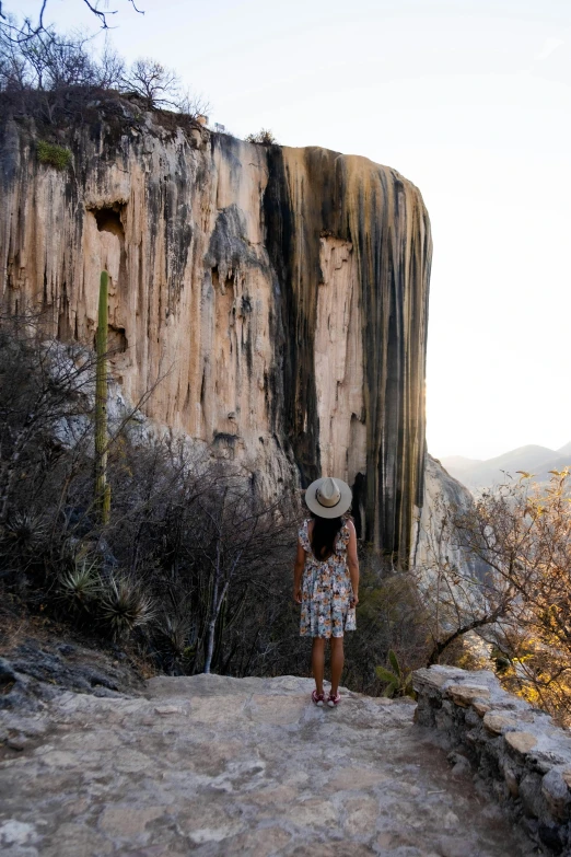 a young woman is standing in the shade with a large rock formation behind her